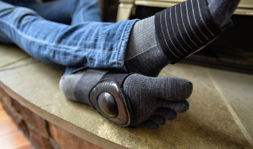 A person, seated on a stone slab, wearing a pair of Black Strutz Pro foot pads