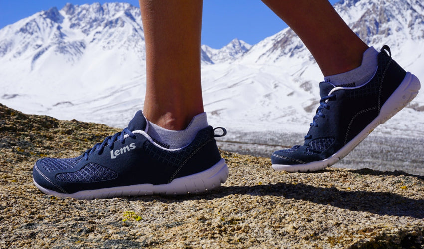 Walker striding over rocky ground in a pair of Lems Primal 2 Eclipse shoes