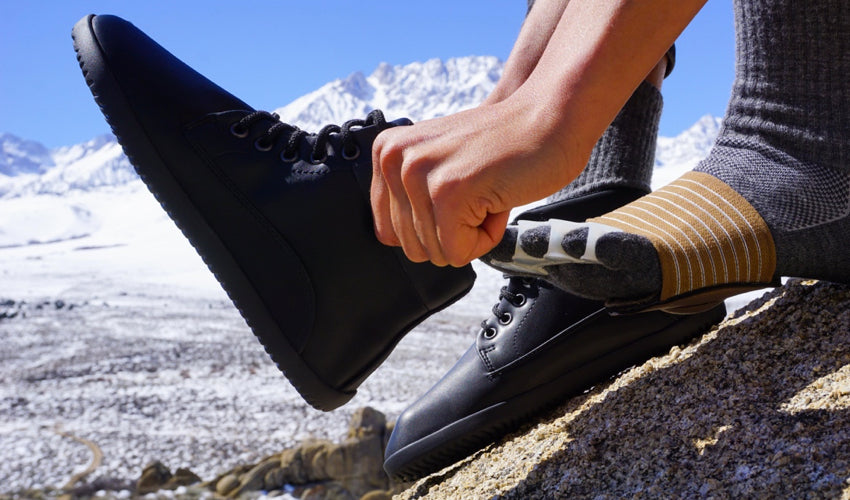 A hiker wearing Strutz Pro Brown foot pads and Correct Toes toe spacing pads putting on Ahinsa Trek Bare Ankle Black boots