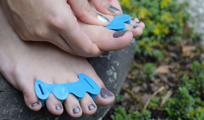 A person putting on a pair of Correct Toes Aqua toe spacers in a garden setting