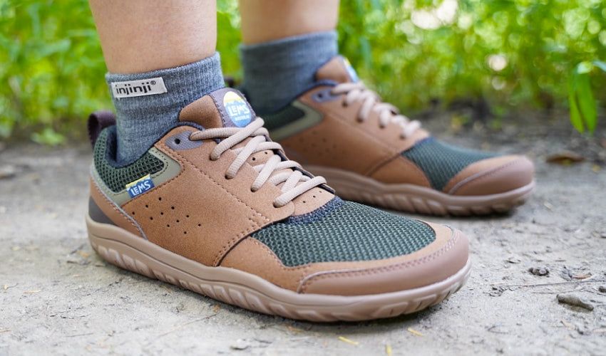 The feet of a person standing solidly in place while wearing a pair of Lems Primal Zen Woodland shoes