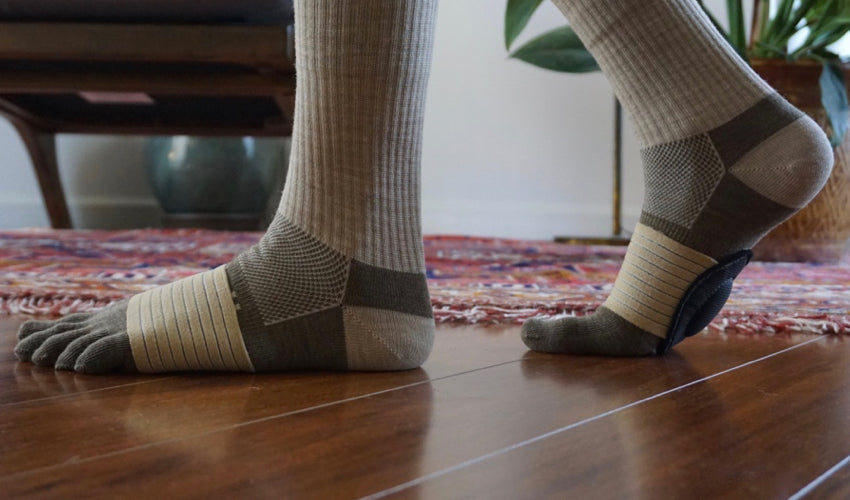 Side view of a person wearing Injinji toe socks and Strutz foot pads indoors, on wood flooring