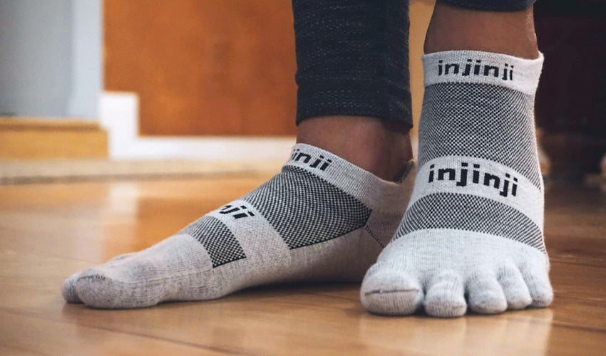Person, with splayed feet, modeling a pair of gray Injinji No Show toe socks