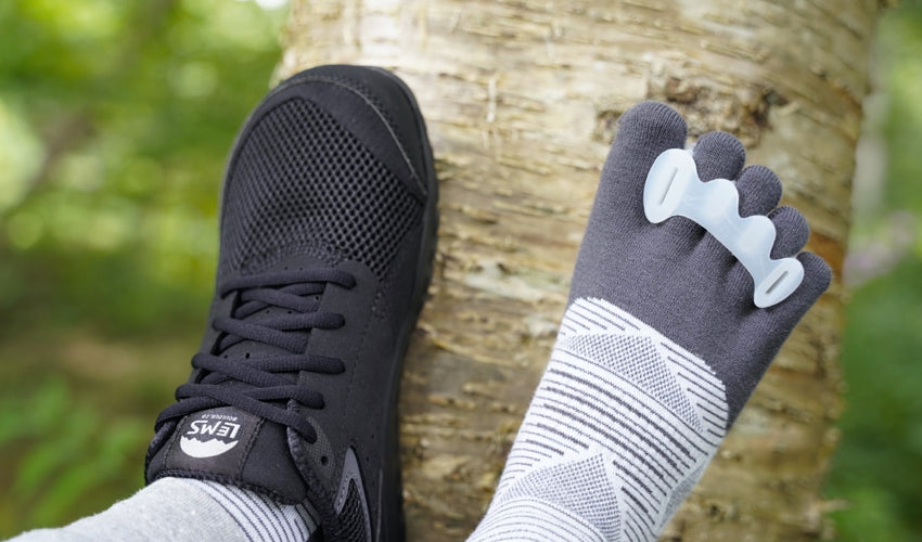 Person wearing Lems Primal Zen Asphalt shoes and Correct Toes Original toe spacers with a birch tree in the background