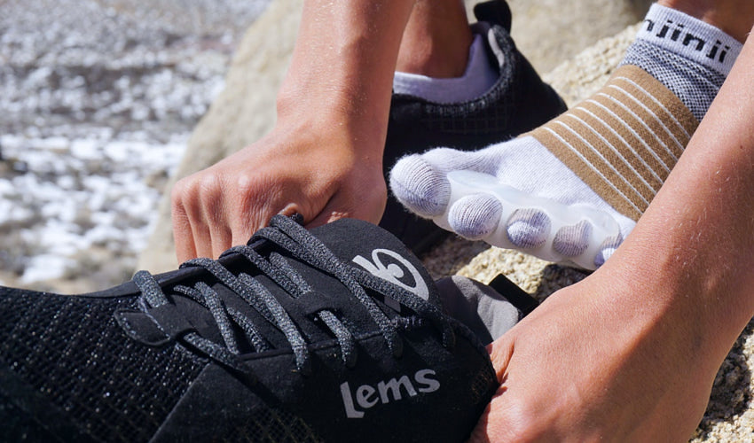 Person donning a Lems Primal 2 shoe while wearing toe spacers, toe socks, and Strutz foot pads