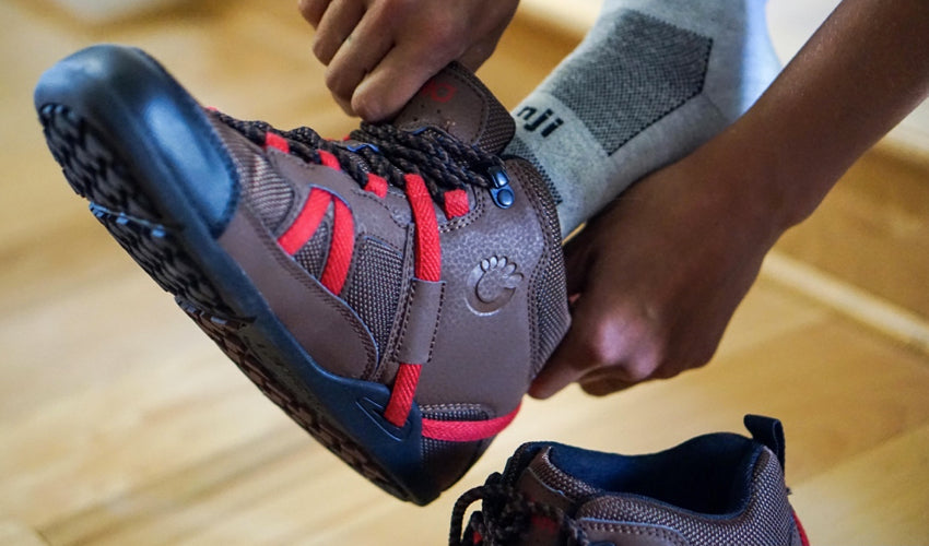 A person, wearing Injinji toe socks, putting on a pair of Xero DayLite Hiker boots