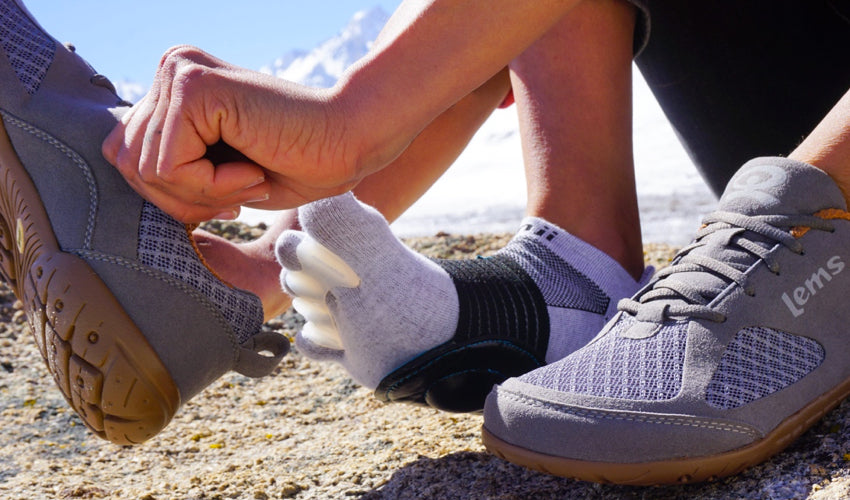 A hiker wearing Correct Toes and putting on a pair of Lems Primal 2 Slate shoes