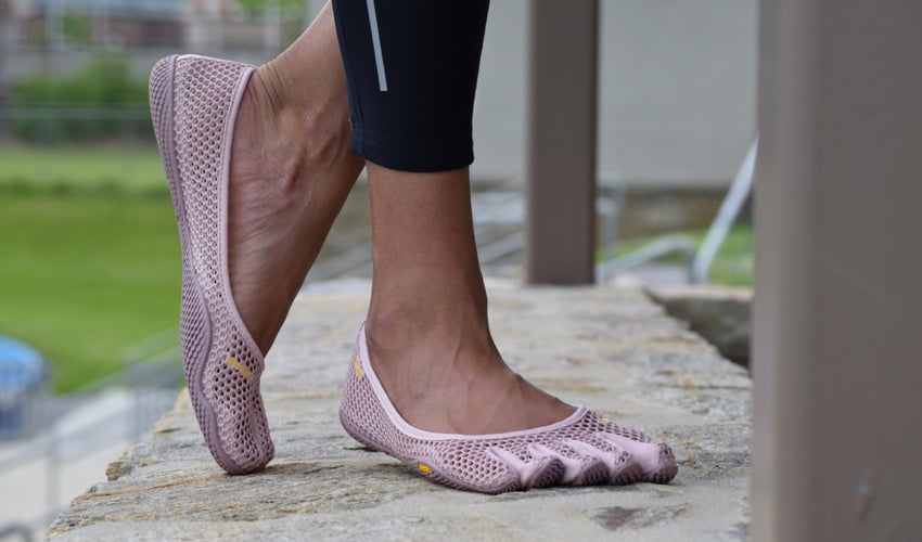 A woman wearing Pink Vibram FiveFingers VI-B shoes and standing on a stone wall