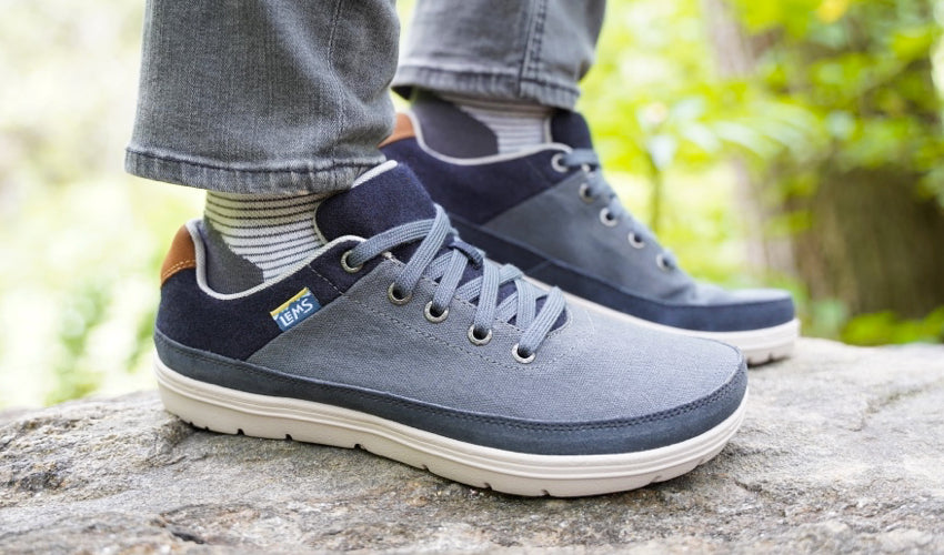 Side view of a pair of Lems Chillum Varsity Blue shoes being worn by a person standing on a rock in nature