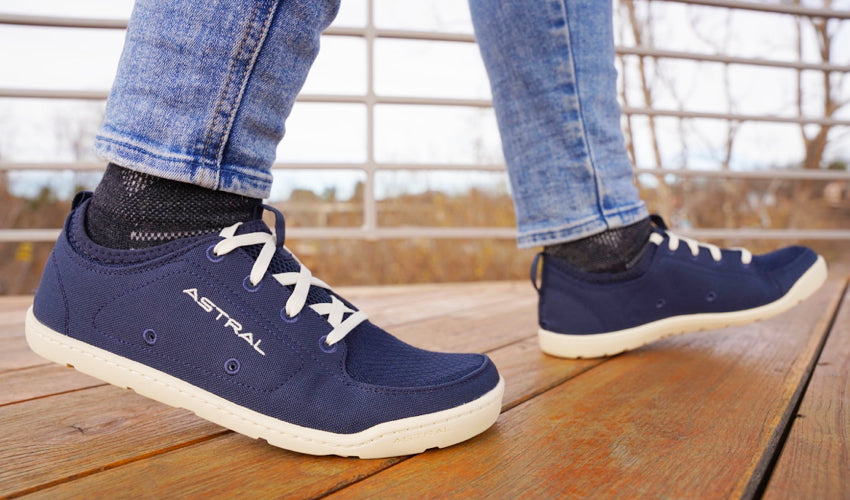 A person in Navy/White Astral Loyak shoes striding across a wood deck