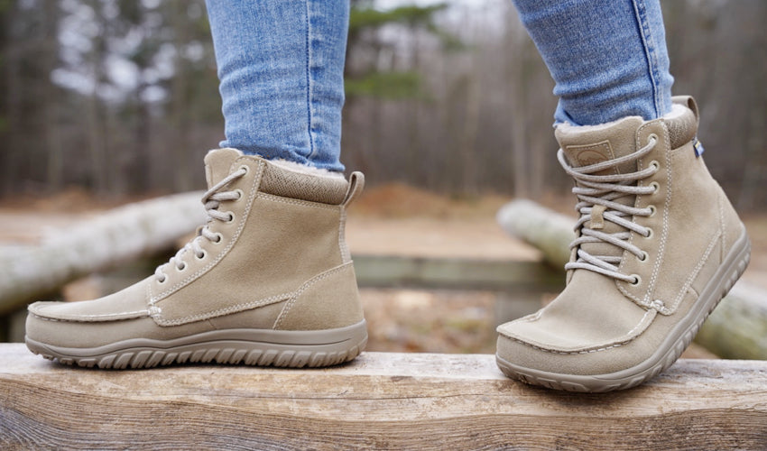 Side view of a person wearing Lems Telluride Boots and standing on a wood beam