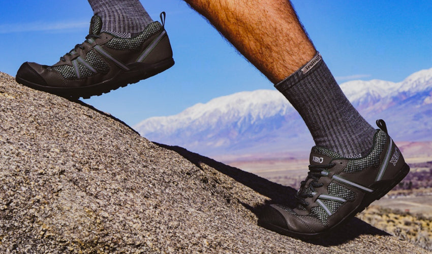 Male hiker wearing Xero TerraFlex trail shoes climbing a boulder with mountains in the background