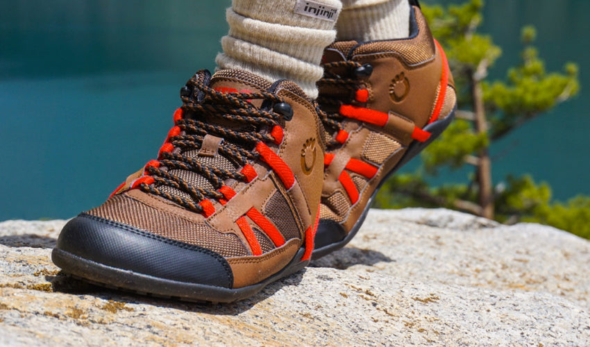 Hiker wearing Xero DayLite Hiker EV boots in Cinnamon Red with green lake in the background