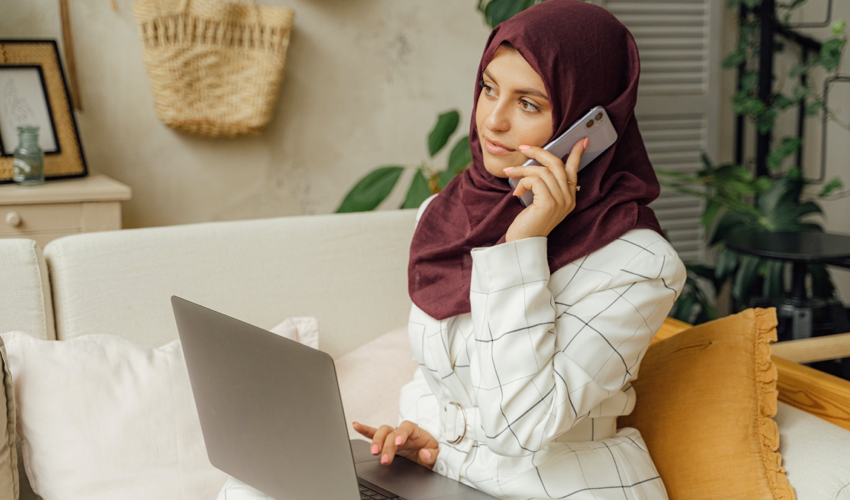 A woman researching her foot care options on a laptop and calling a health care clinic on her cell phone