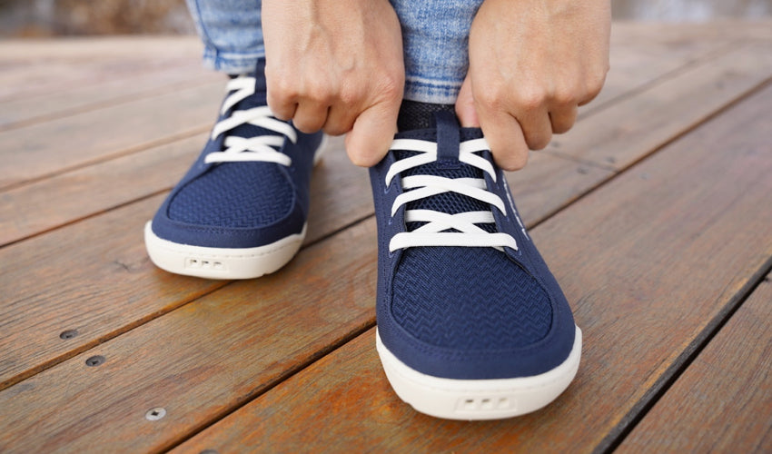 Front view of the hands and feet of an Astral Loyak shoe-wearer who is adjusting the shoe at the ankle