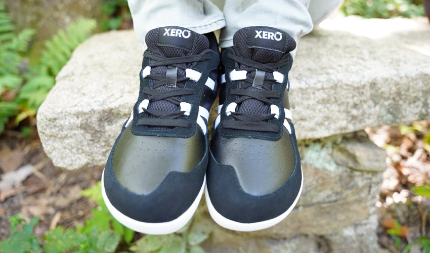 Seated person displaying a pair of Xero Kelso shoes in Black/White