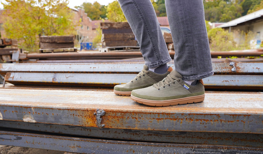 Side view of a person wearing Lems Chillum Spruce casual shoes and standing on a steel beam in an urban environment