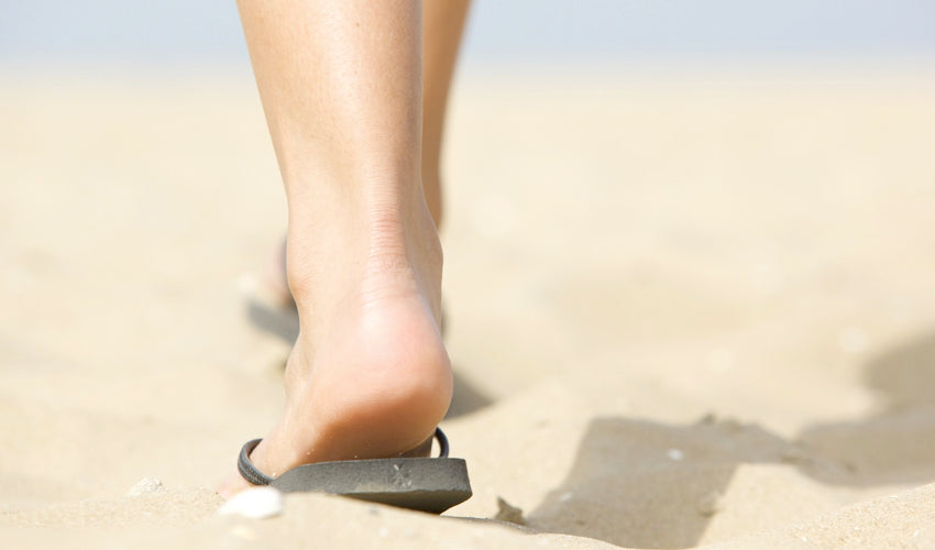 Shot from behind of a person wearing flip-flops and walking over beach sand