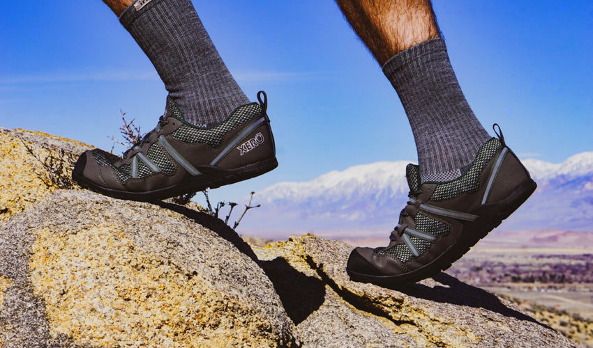 Hiker climbing over rocks and wearing a pair of Xero TerraFlex Black trail shoes