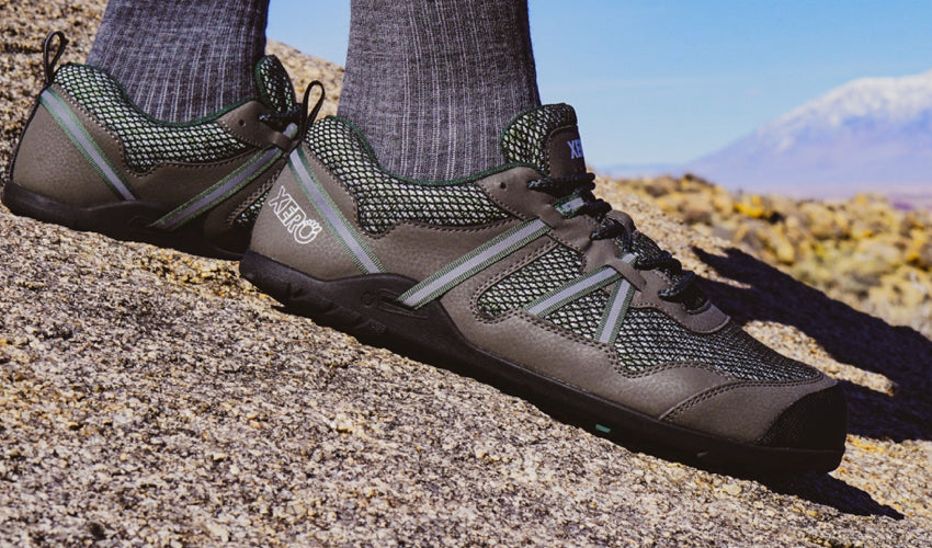 Person wearing Xero TerraFlex Forest trail shoes and sitting on a large rock with mountains in the background