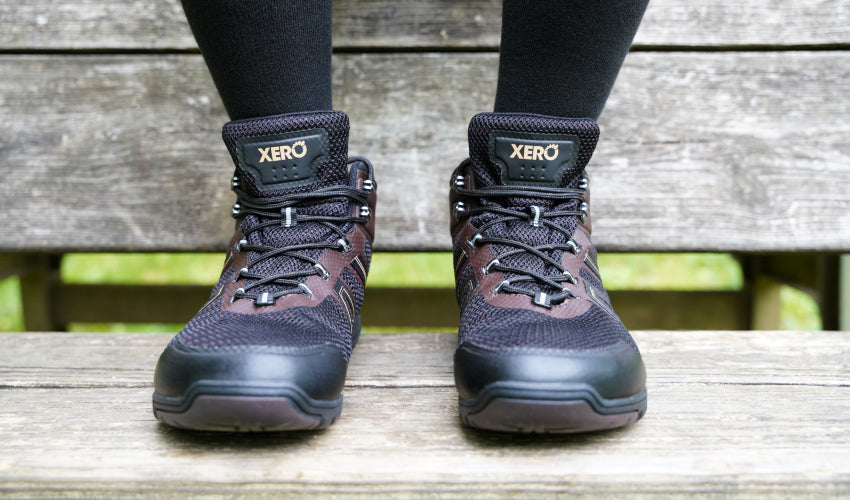 Hiker sitting on a wooden bench and sporting a pair of Xero Xcursion Fusion hiking boots in Bison