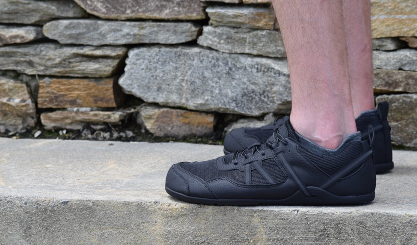 Man in a pair of flat-soled Xero Prio Black athletic shoes standing on a concrete step