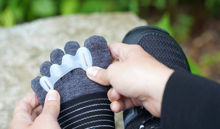 Over-the-shoulder view of a person donning a Correct Toes Original toe spacer over an Injinji toe sock