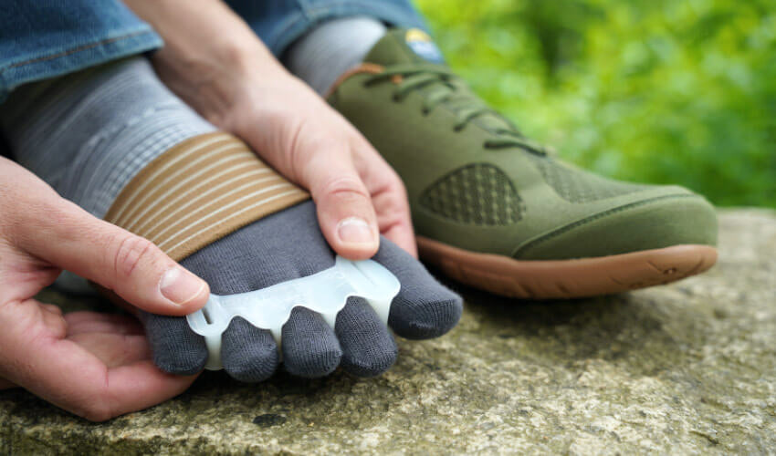 Side view of a person gently maneuvering a pair of Correct Toes Original toe spacers into place over a pair of Injinji toe socks