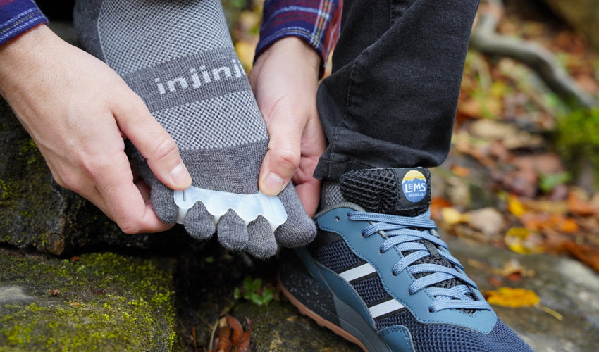 Person seated in the woods and wearing a flannel top donning a Correct Toes Original toe spacer