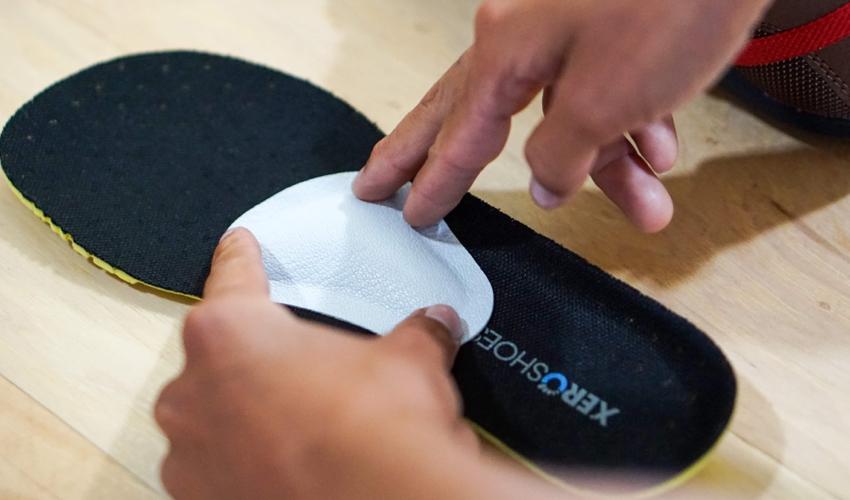 A close-up image of a person affixing a Pedag metatarsal pad to a shoe insole