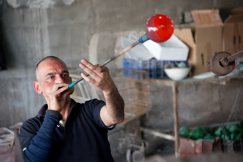 A glass blowing artisan with Hebron Glass shown blowing a new art piece from recycled glass. 