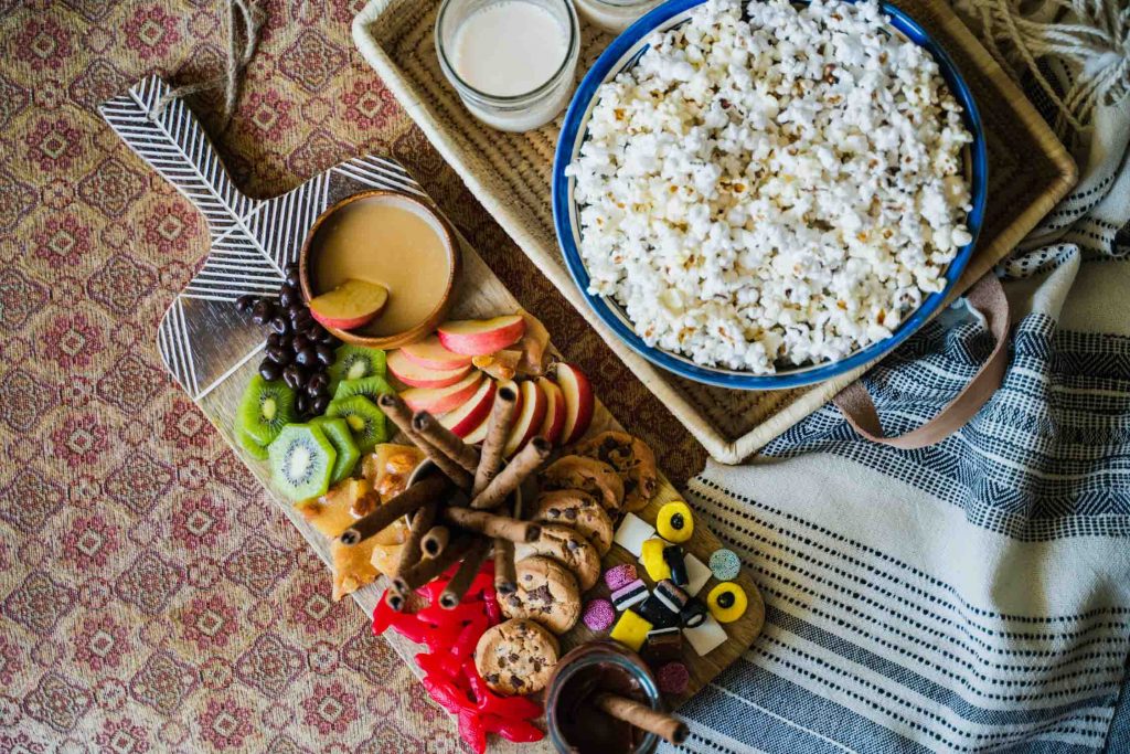 The Movie Night Board is an epic charcuterie board built on the Minimalist Serving Board from Ten Thousand Villages. Fruits, candies and cookies adorn the board next to the Rectangle Handled Basket that hosts a bowl of popcorn in the Bouquet Bowl. 