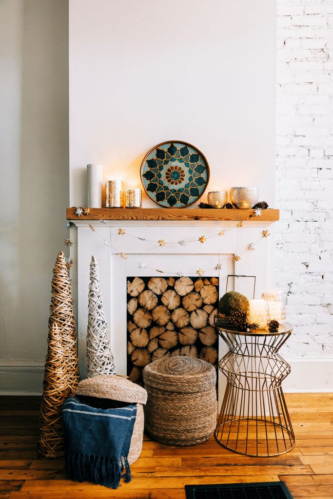 Image shows a Winter Solstice styled mantle with a medieval painted tray as the anchor piece, candles, garlands, baskets abound. 