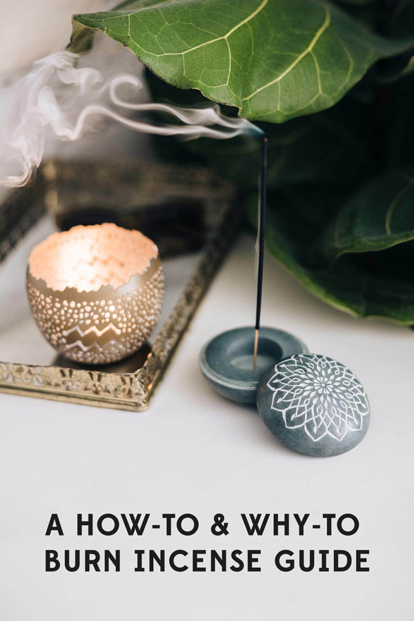 A tranquil scene in which a stick of incense burns, smoke curling up from the Stone Incense and Candleholder from Ten Thousand Villages. Placed near a fiddle leaf fig leaf and a handcrafted zodiac candleholder. 