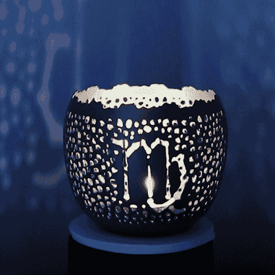 Gif of fair trade, handcrafted Zodiac candleholder with the VIrgo sign in the punchwork spinning slowly; casting light patterns on the indigo walls around it. 