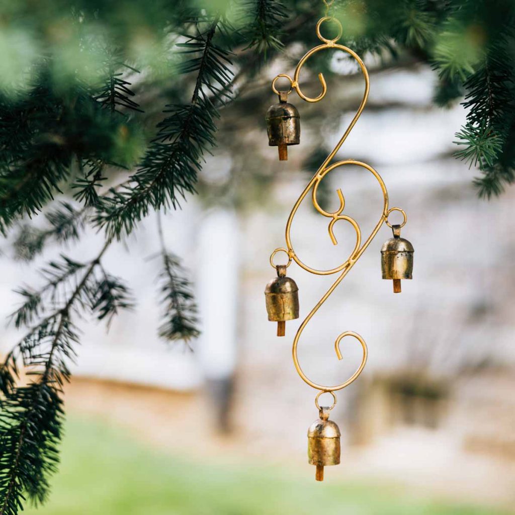 curly cue brass bells hanging from a pine