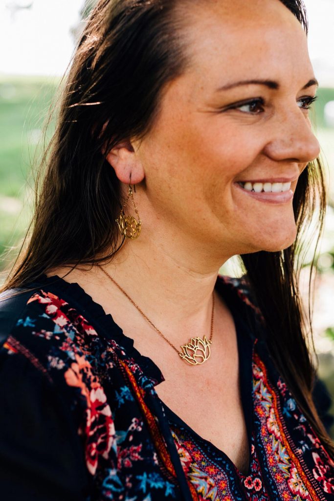Bombshell Jewelry pieces, The Graceful Lotus earrings, and The Graceful Lotus necklace are pictured on a model with long dark hair. She is smiling and looking off in the distance. 