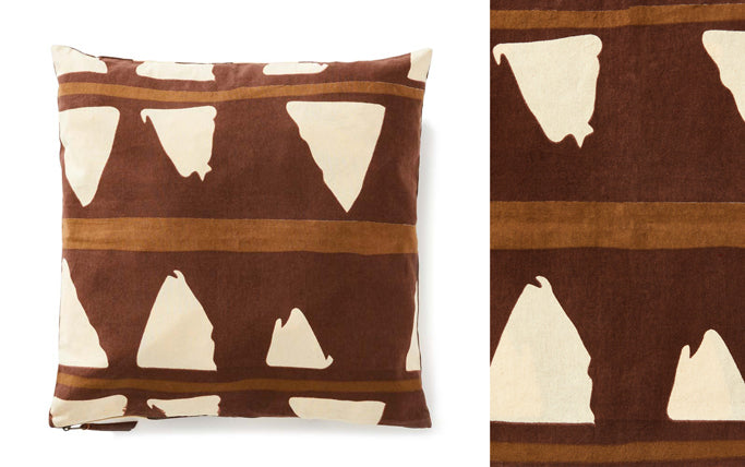 The Roar Pillow with its white triangle tooth patterns on a brown background. It is an elevated take on a toothy design. 