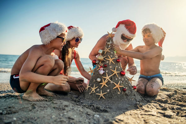 Family building a sand Christmas tree on the beach.