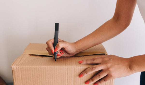 Person labeling a cardboard box with a black marker.