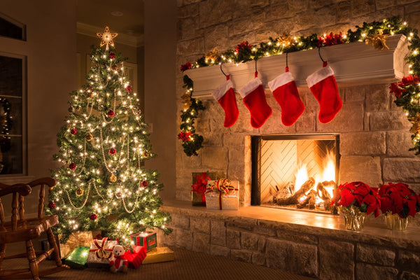 Lit Christmas tree with stockings by a stone fireplace.