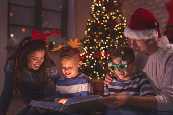 Family reading a book by a lit Christmas tree.