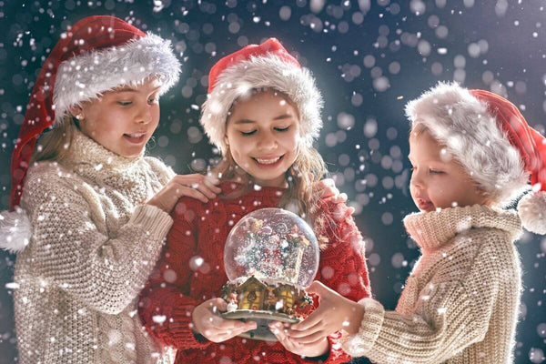 Three kids in Santa hats admiring a snow globe.