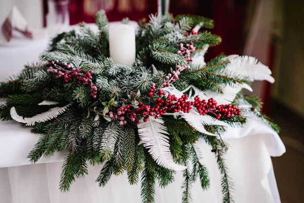 Festive table centerpiece with candle, pine branches, and berries.