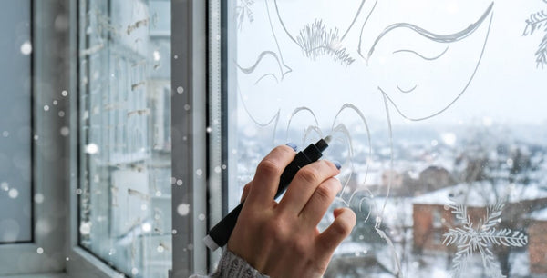 Hand drawing festive patterns on a frosty window with a snowy view.