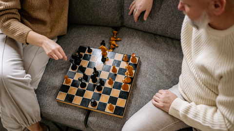 två personer spelar schack i grå soffa closeup