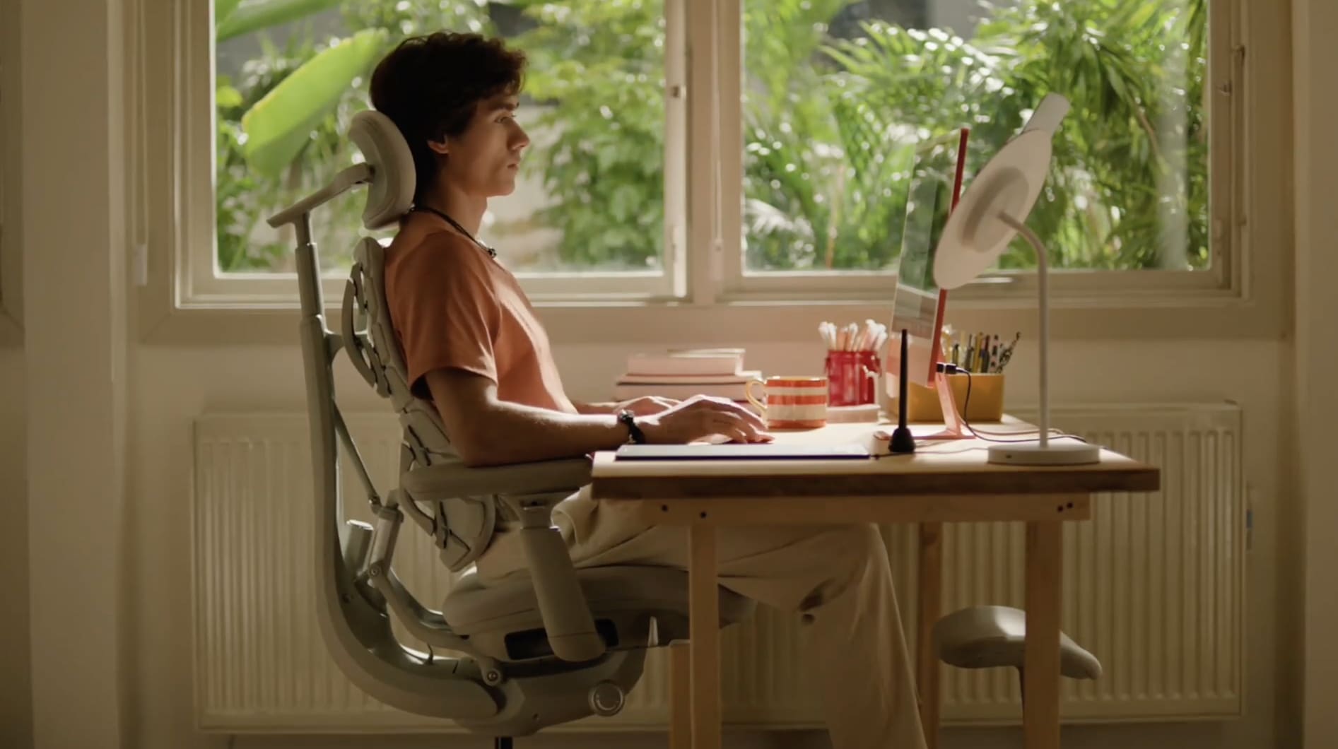 Man sitting upright in an ergonomic chair at a desk, focusing on work in a bright home office.