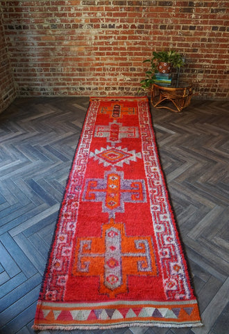 11 foot by 3 foot Herki Turkish runner with beautiful deep red pile as the main color, border on each side with triangles in orange, purple, light blue and cream and large medallions in the center