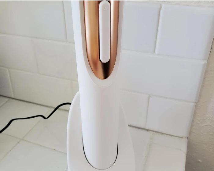 White and rose gold hand dryer on a tiled wall with a power cord.