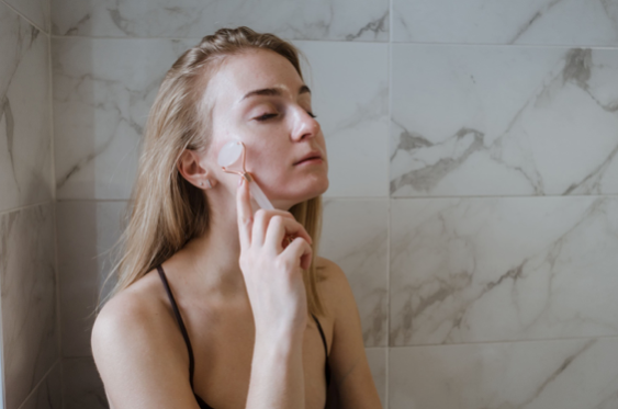 Une jeune femme se trouve dans la salle de bain, elle utilise un roller en pierre sur son visage pour le sculpter et le garder ferme.